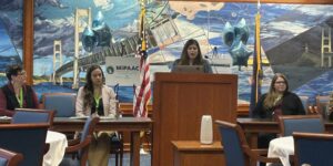 Person standing at a podium speaking to a room of tables